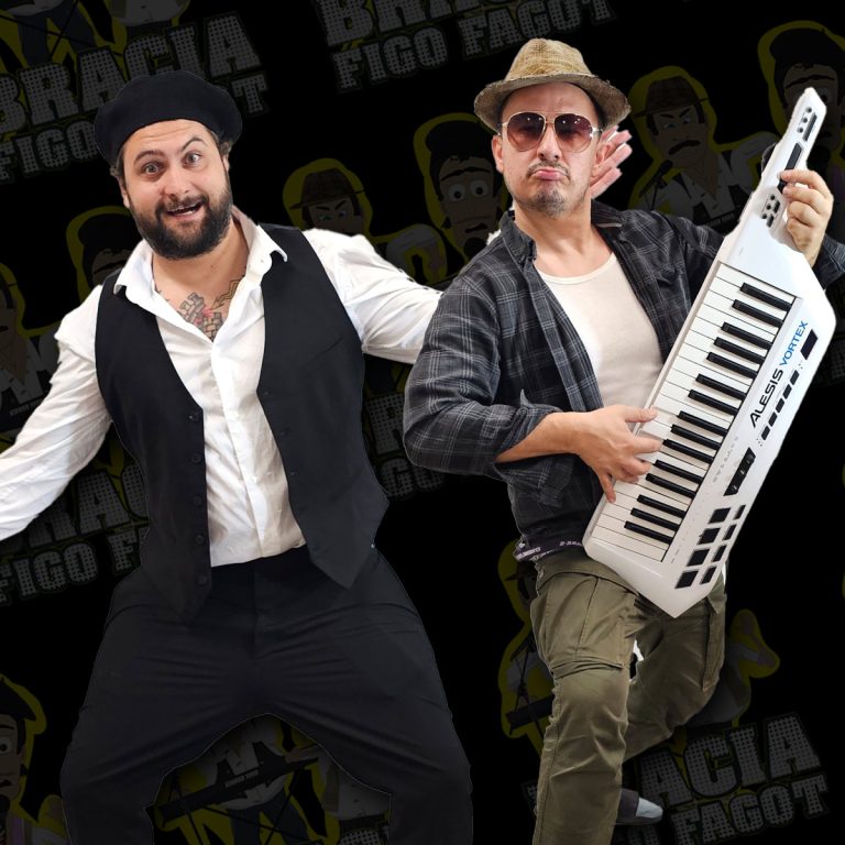 Dwóch mężczyzn na czarnym tle z graficznym wzorem. Jeden ubrany w białą koszulę, czarną kamizelkę i beret, wykonuje energiczny gest taneczny. Drugi ma na sobie kapelusz, okulary przeciwsłoneczne i koszulę w kratę, trzyma biały keytar. Obaj pozują dynamicznie, w koncertowym klimacie.